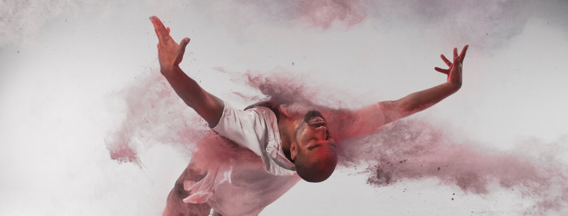 one contemporary male dance performer leaning right back from the waist with clouds of coloured dust erupting around them  